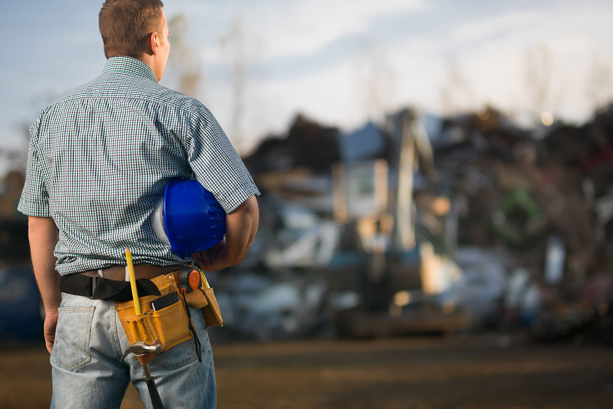 Person holding a helmet, overlooking an industrial work site.