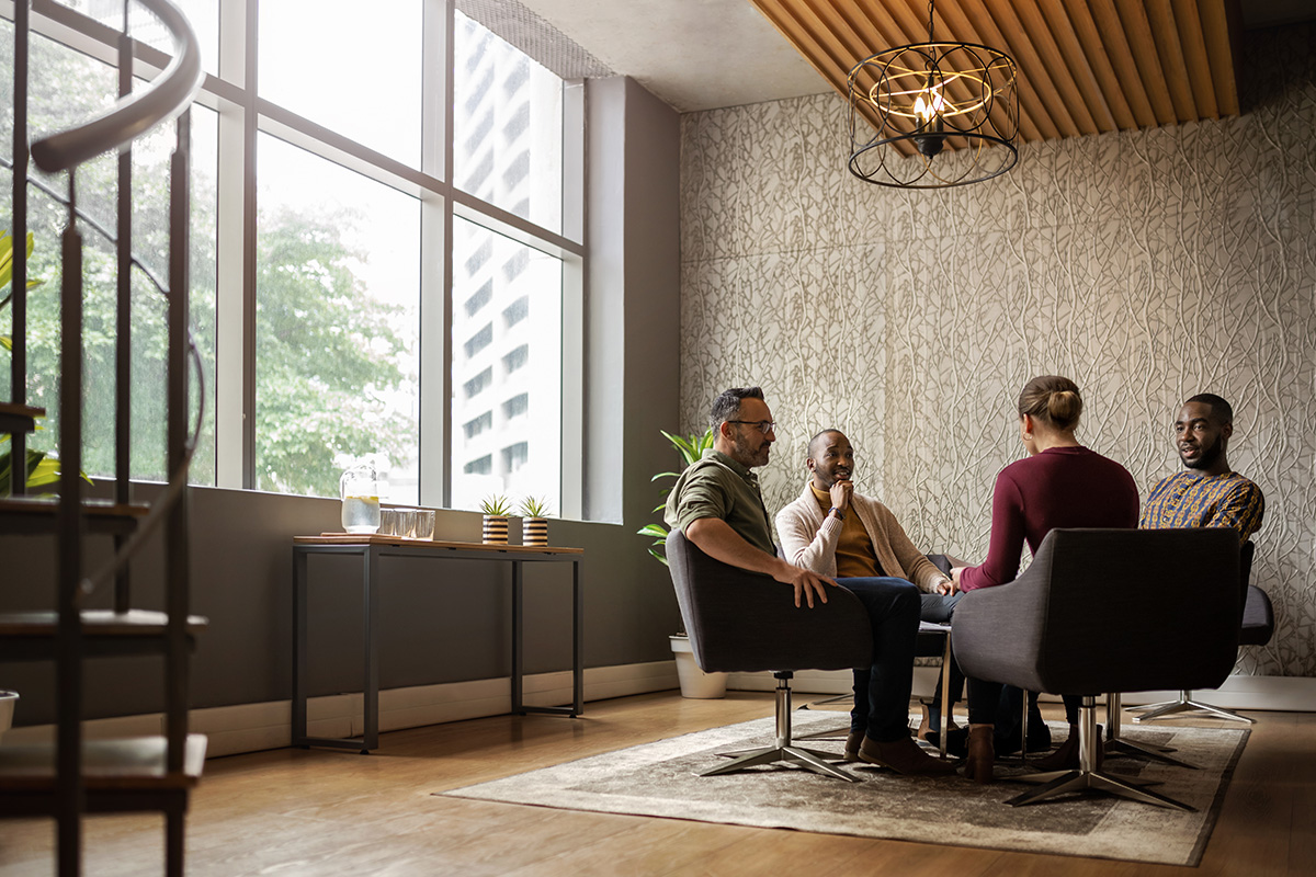 Four individuals seated in chairs engaged in a business discussion during a meeting.