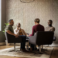 Four individuals seated in chairs engaged in a business discussion during a meeting.