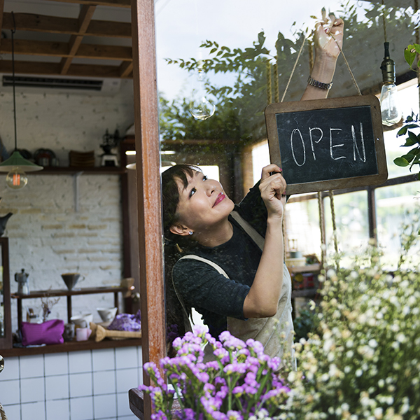 Shop owner flipping a closed sign to open in front of a charming boutique store.