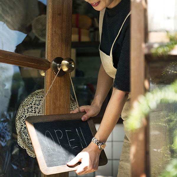 Shop owner holding an open sign in front of a small business.